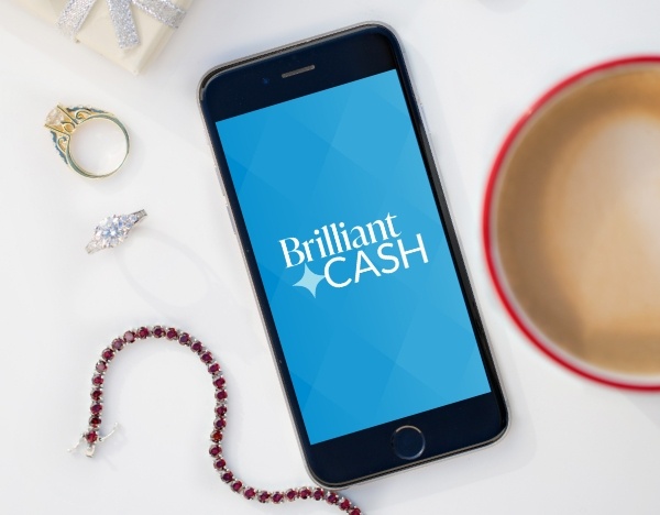 Brilliant Cash logo on a mobile phone surrounded by assorted jewelry and a coffee cup 